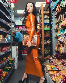 Full-body shot of a model walking down a grocery aisle in an orange latex dress holding a box of biscuits