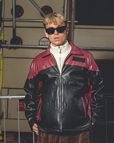 Male model in a burgundy and black leather jacket and corduroy trousers against metal scaffolding