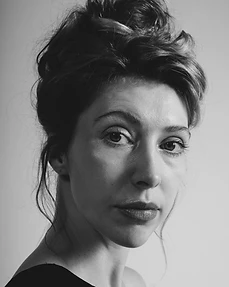 Black and white chest-up portrait of a woman with a voluminous updo in a dark off-shoulder top