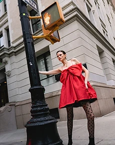 Model in a red dress leaning against a traffic signal pole at a street corner