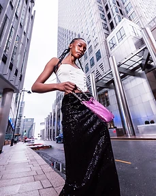 Model in a white corset and black sequin skirt holding a pink bag beneath glass skyscrapers