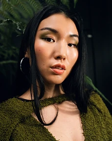 Close-up portrait of a model in an olive-green knit top framed by dark fern fronds