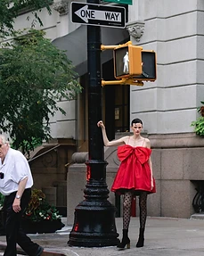Model in a red dress with a large bow leaning on a street lamp post