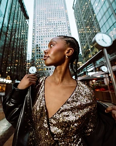 Profile portrait of a model in a gold sequin top and leather jacket with a city clock at dusk behind