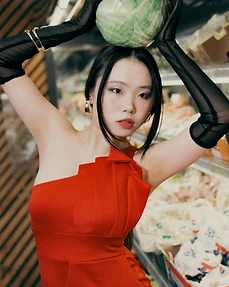Model in a red dress lifting a cabbage above her head among grocery shelves