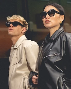 Medium close-up of two models linked arm in arm in leather jackets against reflective glass