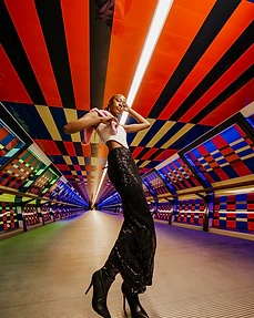 Model in a white corset, black sequin skirt and pink fur stole posing in a brightly coloured geometric tunnel