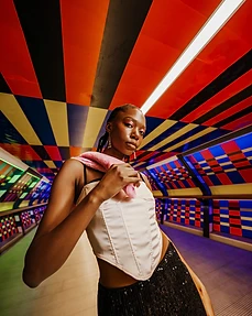 Medium portrait of a model in a white corset and pink shawl under a multi-coloured tunnel ceiling