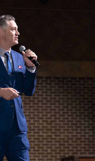 Joe Sallustio addressing an audience against a brick wall backdrop
