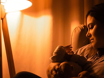 A parent cradling a newborn by lamplight