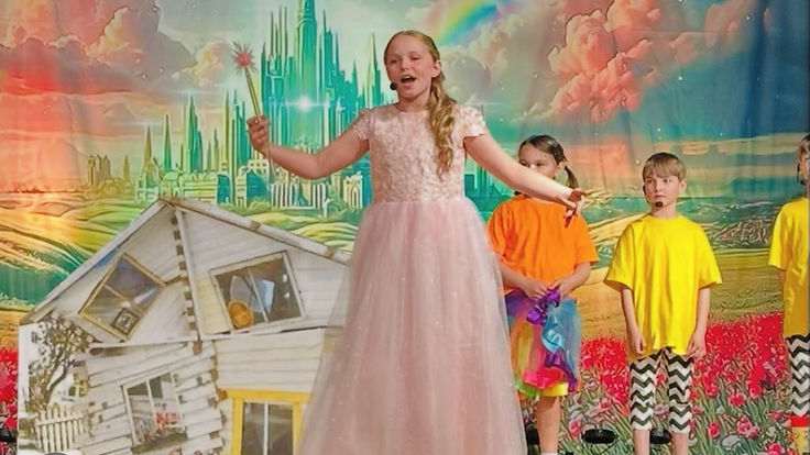Young Annie Jr. performer in a pink gown holding a star wand on a fantastical stage set
