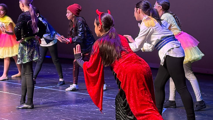 Annie Jr. performers in colorful character costumes under a brick-wall projection
