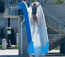Showstoppers camper splashing down a water slide on a summer camp day