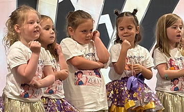 Five young performers in gold skirts posing before an Art Deco backdrop