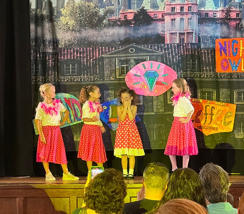 Showstoppers performers in polka-dot dresses on a city-street stage set