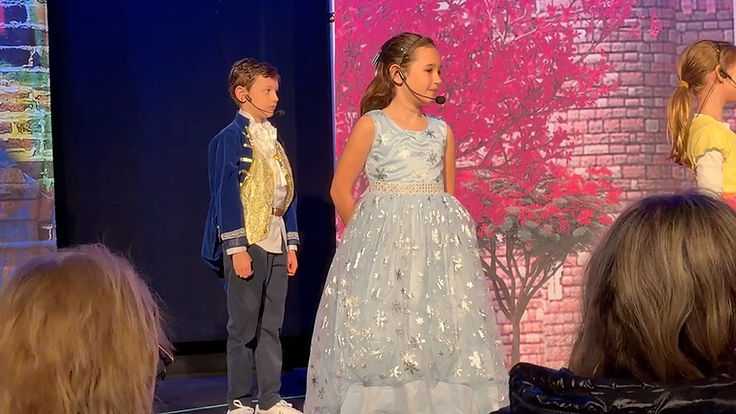 Two young Annie Jr. performers in a butler and ballgown scene under a cherry blossom backdrop
