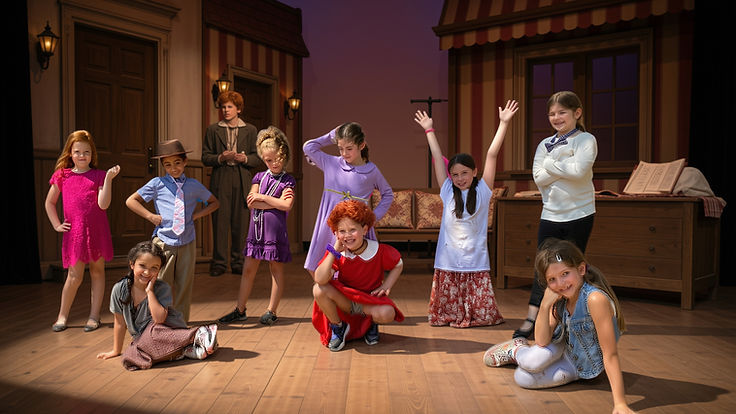 Annie Jr. cast in costume on a street set with storefronts and awnings