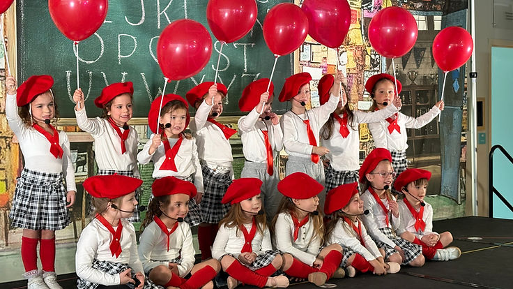 Annie Jr. classroom scene with children holding red balloons in front of a chalkboard backdrop