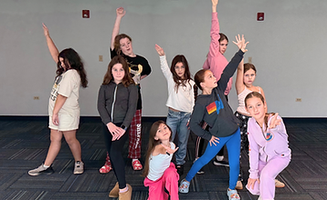 Performers in a rehearsal room with arms raised in a synchronized pose
