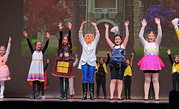 Cast in costume taking a final bow on stage with a brick-building backdrop