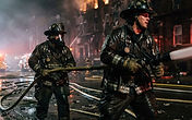 Firefighters in turnout gear working a hose line at a multi-story apartment building fire at night, symbolic editorial photograph for USPA Nationwide Security newsroom