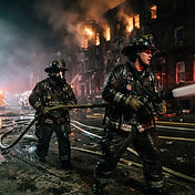Firefighters in turnout gear working a hose line at a multi-story apartment building fire at night, symbolic editorial photograph for USPA Nationwide Security newsroom