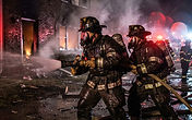 Firefighters in turnout gear operating at night outside a two-story apartment building, emergency lights illuminating the scene