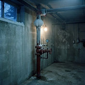 Frost-covered red fire sprinkler riser and handwheel valve in an unheated commercial basement during a hard freeze