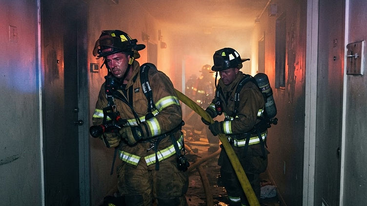 Miami firefighters in turnout gear advancing a hose line through a smoke-filled residential building corridor during a multi-story apartment fire response
