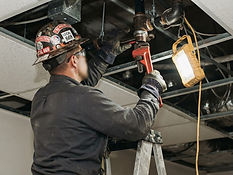 Licensed fire protection technician replacing a fractured sprinkler pipe section above a commercial ceiling in Dallas, TX - USPA Nationwide Security
