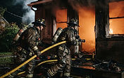 Firefighters in turnout gear advancing a handline into a smoke-filled apartment building doorway during a structure fire response