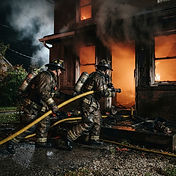 Firefighters in turnout gear advancing a handline into a smoke-filled apartment building doorway during a structure fire response