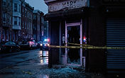 Shattered glass storefront door taped off by police on a Baltimore commercial street before dawn, illustrating the Remington business burglary spree