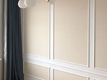 Boiserie branca com painéis em tom areia vestindo a parede de sala clara com lustre dourado