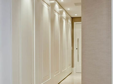 Corredor com painéis boisérie brancos em portas altas e iluminação embutida