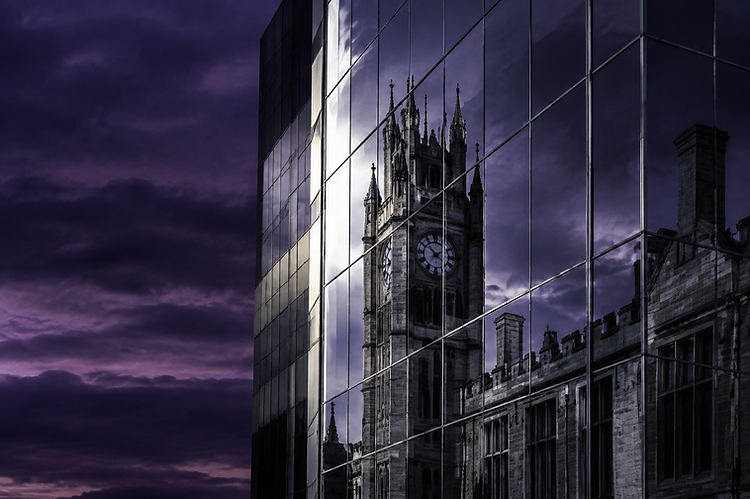 Modern glass architecture reflecting a collegiate stone clock tower