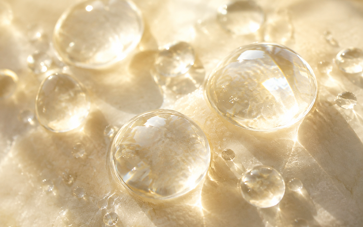 Macro photograph of dewdrops resting on a pale stone surface