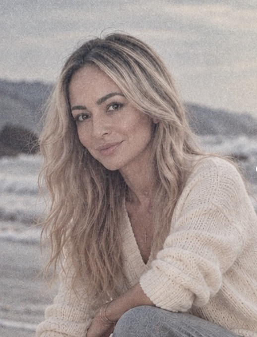 Ashley Powell smiling, seated at the shoreline