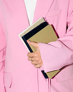 Person in a pink blazer holding a stack of notebooks