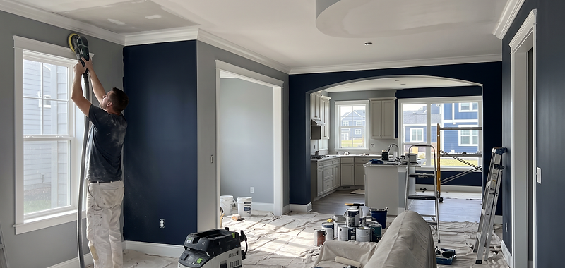 A painter sanding a freshly patched wall inside a lit room