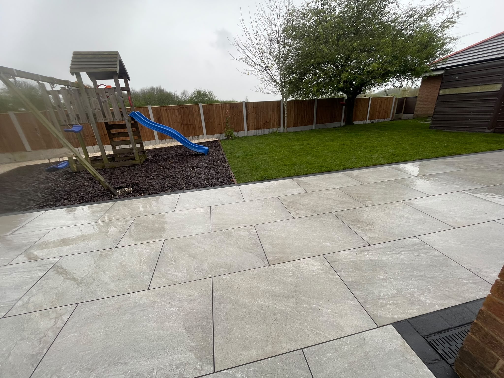 Grey porcelain patio with play area and lawn