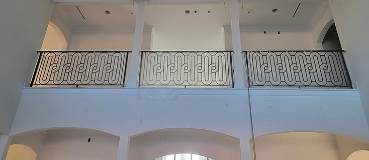 Ornamental scroll-pattern iron balcony railing over a great room, fabricated by RF Iron Works