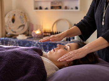 A Reiki practitioner's hands hovering above a relaxed client lying with eyes closed beneath a deep purple blanket.