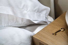 White linen bedding beside a brass key on an oak bedside table in soft morning light
