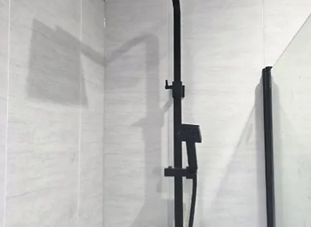 Matte black rain shower head and thermostatic valve in a tiled shower enclosure