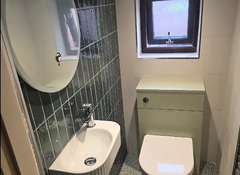 Bathroom with dark green tiled wall, round mirror, wall-hung basin and concealed cistern