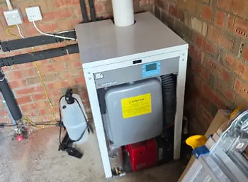 Floor-standing boiler installed against a brick wall with its flue running up to the ceiling