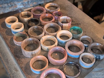 Around thirty finished wooden rings laid out on a dark bench in front of a stack of rough planks