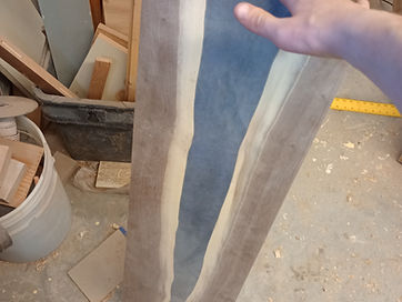 A live edge river blank with a blue-grey resin channel held up in the workshop