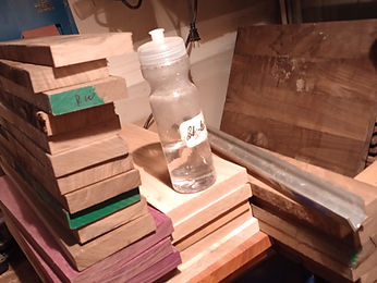 Cut blocks of figured and pale hardwood stacked on the bench beside sanding sheets and pliers
